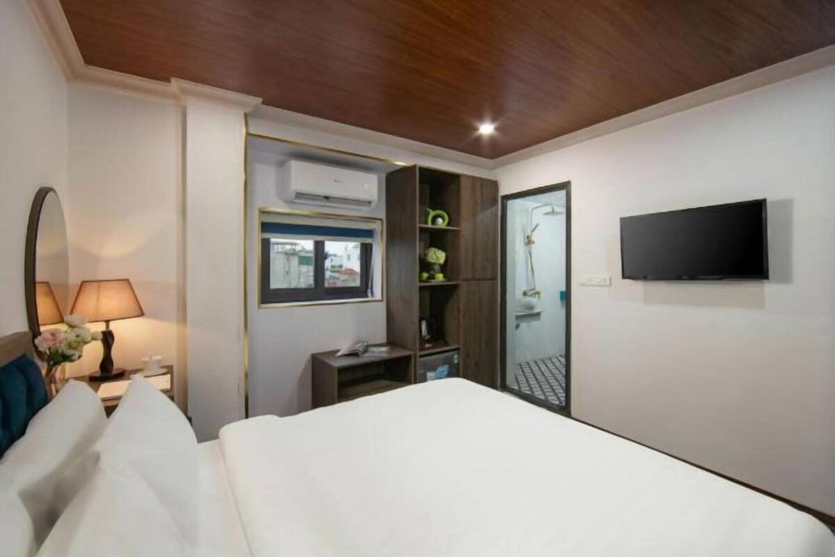 A hotel room with a bed, a TV, a window, a door, and a wall-mounted air conditioning unit.