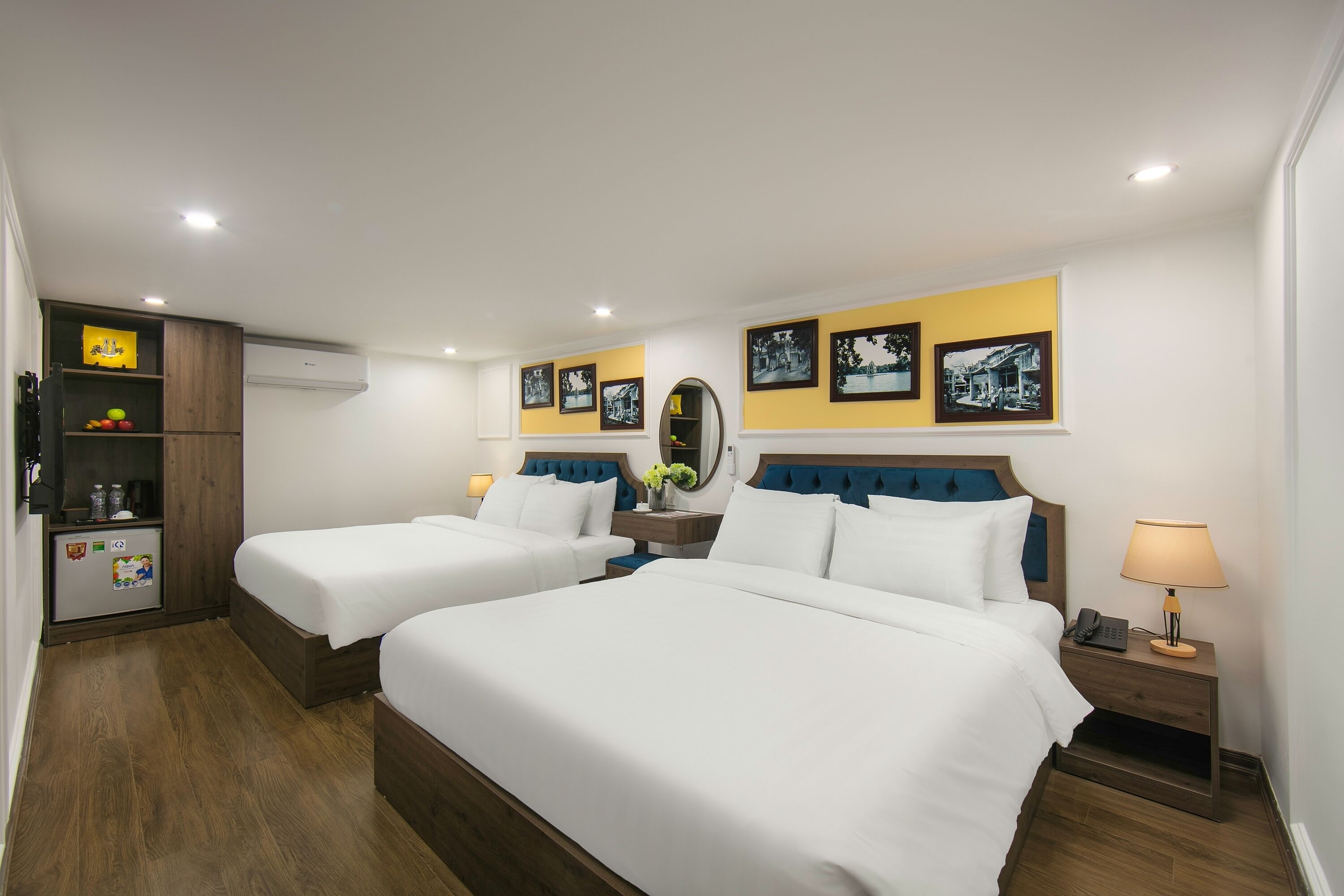 Habitación de hotel con dos camas, un pequeño kitchenette, un espejo y cuadros en la pared.