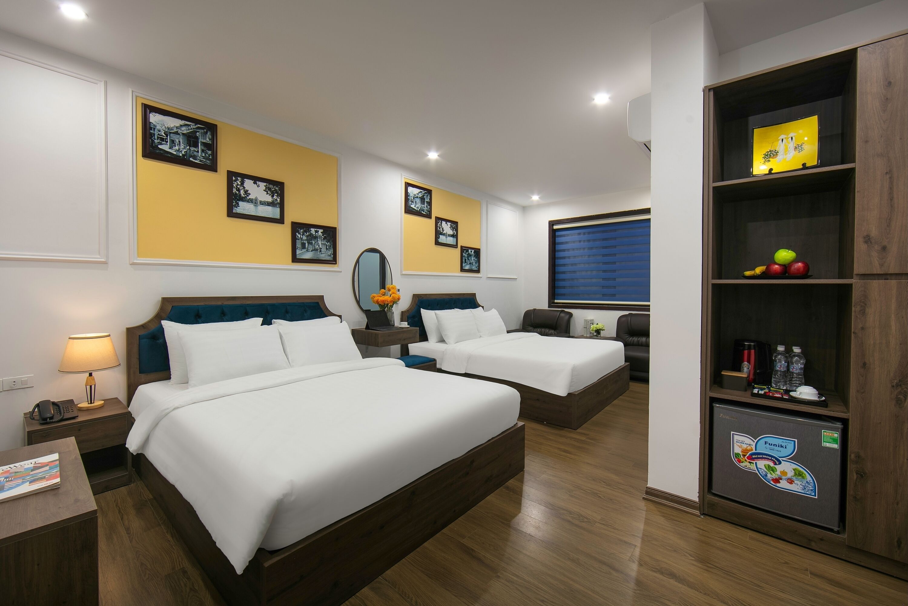 Habitación de hotel con dos camas, un escritorio, una mesita de noche, un espejo y una repisa con botellas.