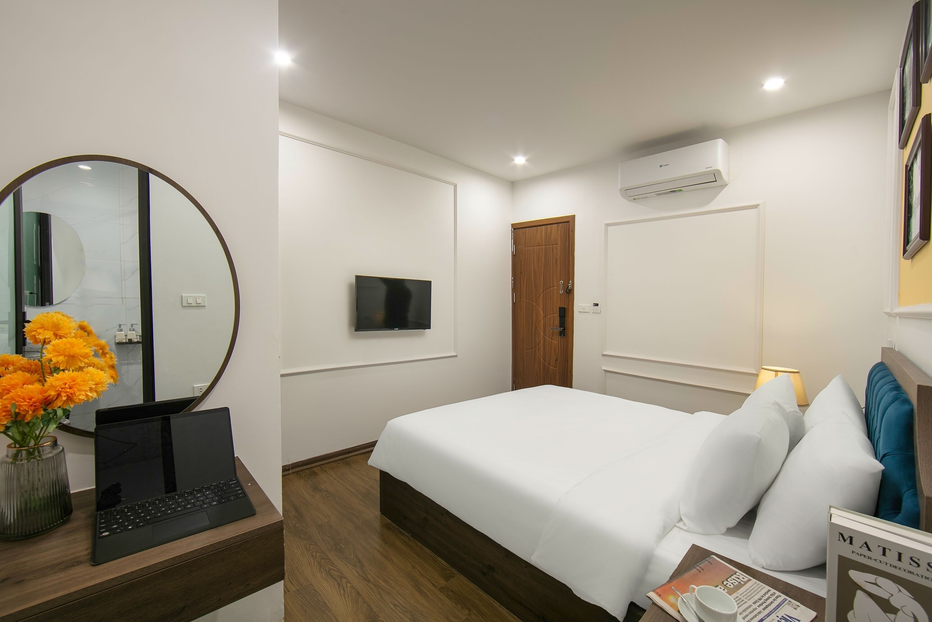 A hotel room with a bed, a desk with a laptop, a TV, and a mirror.