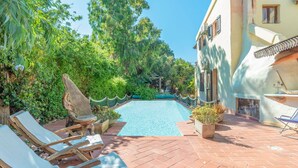A pool area with lounge chairs, a stone sculpture, and lush greenery.