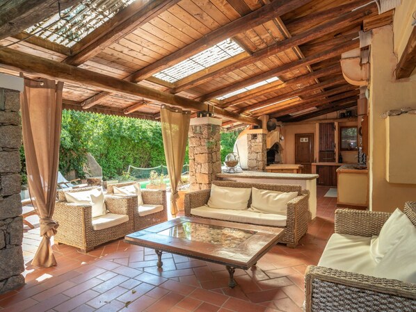 An open-plan living area with wicker furniture, a stone wall, and a kitchen in the background.