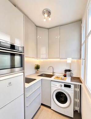 A compact kitchen with a built-in oven, a sink, a coffee machine, and a washing machine.