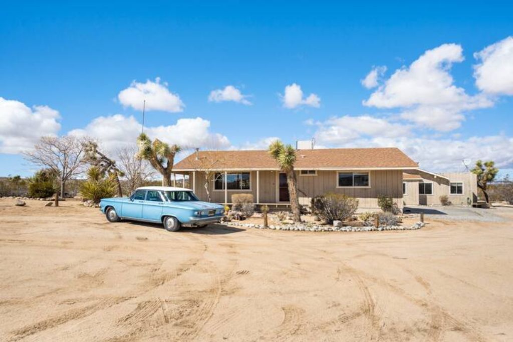 Una casa nel deserto con un'auto blu parcheggiata davanti.