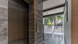 A modern elevator with a marble wall, a staircase leading to an outdoor area, and a clean, minimalist design. - Luxury Polanco Apt w/ Wine Cellar & Views (Ciudad de México)