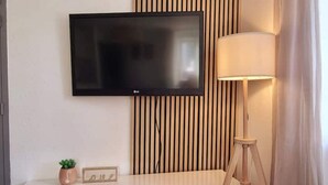 A modern room with a flat-screen TV mounted on the wall, a bedside table with a lamp, and a small potted plant. - le 31 - Mulhouse Pfastatt (Pfastatt)