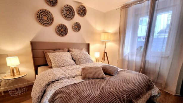 A bedroom with a bed, a bedside table with a lamp, a floor lamp, and a window with curtains. - le 31 - Mulhouse Pfastatt (Pfastatt)