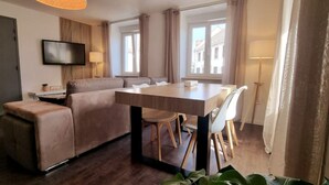 A modern living room with a sofa, a dining table, and chairs. There is a TV mounted on the wall and a lamp on a side table. - le 31 - Mulhouse Pfastatt (Pfastatt)