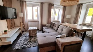 A modern living room with a sectional sofa, a dining table, and a TV mounted on the wall. - le 31 - Mulhouse Pfastatt (Pfastatt)