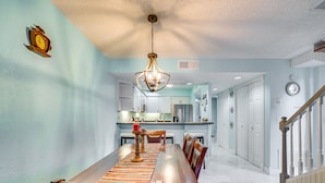 A dining area with a long wooden table, chairs, a hanging light fixture, and a kitchen in the background. - Waterfront Inverness Retreat w/ 3 Boat Ramps (Inverness)