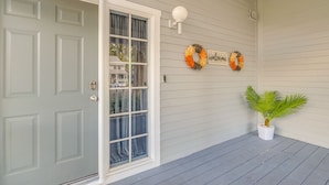 A house with a white door, a window with curtains, a porch with a potted plant, and two wreaths on the wall. - Waterfront Inverness Retreat w/ 3 Boat Ramps (Inverness)