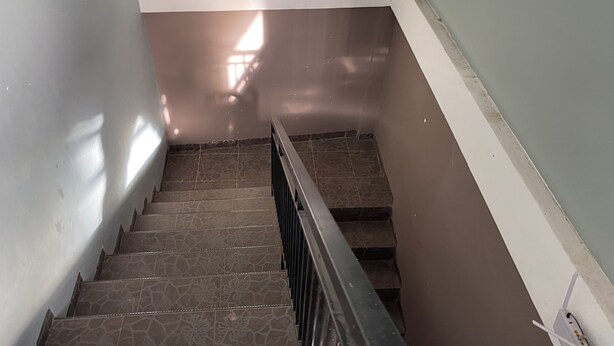 A staircase with a handrail, leading to a landing with a light switch and a power outlet. - Hotel O Mely Homestay (Kendari)