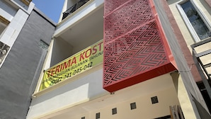 A building facade with a prominent red geometric pattern and a yellow sign advertising a property for sale. - Hotel O Mely Homestay (Kendari)