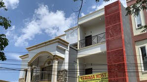 A multi-story building with a prominent red and beige facade, a balcony with black railings, and a banner advertising a business. - Hotel O Mely Homestay (Kendari)