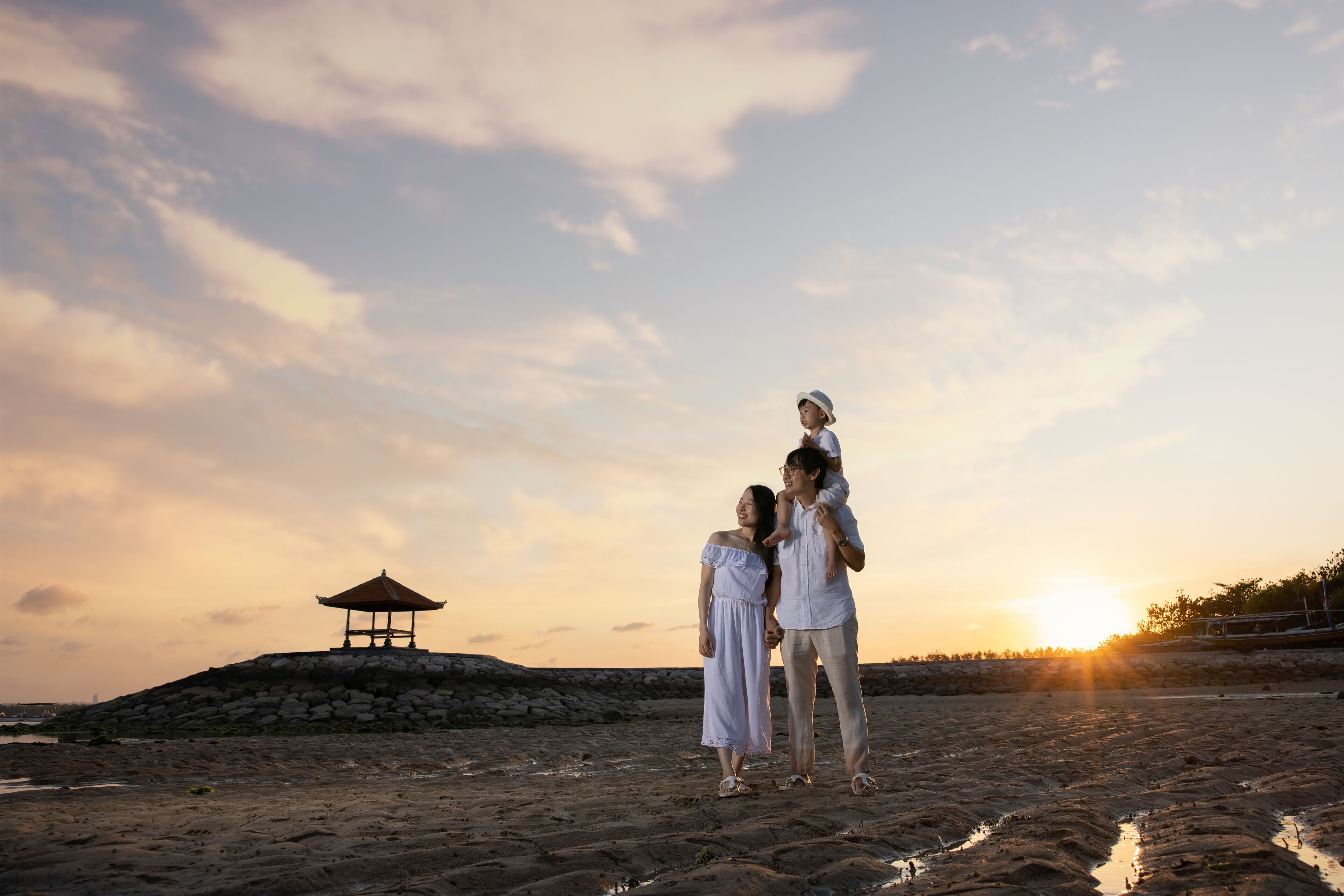 A beach scene with a gazebo, a sunset, and a family.