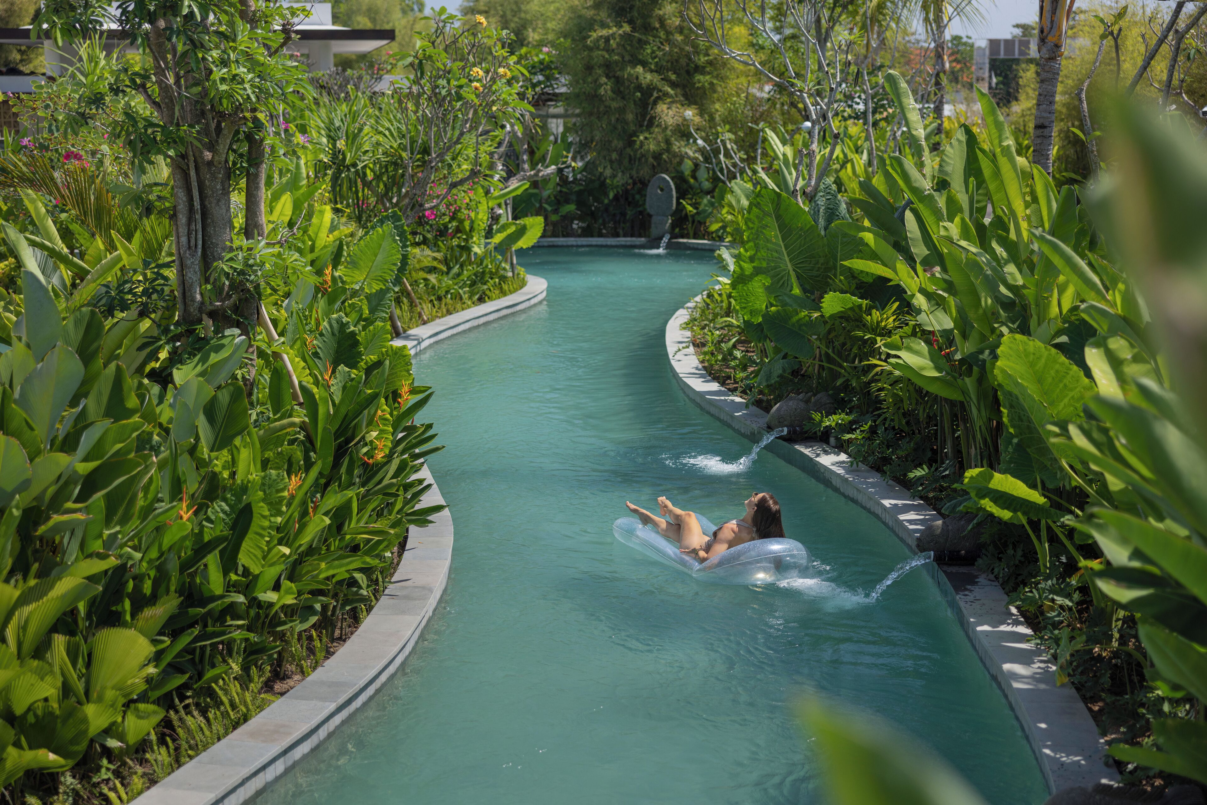 Ein Pool mit geschwungener Kante, umgeben von üppiger Bepflanzung und einem klaren, blauen Wasserspiel.