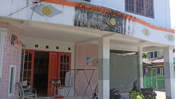 A two-story building with a covered porch, a motorcycle parked outside, and a small garden area with flowers.
