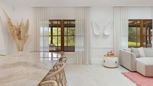 Ein modernes Wohnzimmer mit einem Marmoreßtisch, weißen Sofas und großen Fenstern mit Vorhängen.