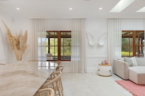 Ein modernes Wohnzimmer mit einem Marmoreßtisch, weißen Sofas und großen Fenstern mit Vorhängen.