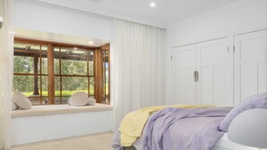Ein Schlafzimmer mit einem großen Fenster, einem Bett mit gelb-lila Decke und weißen Wänden.