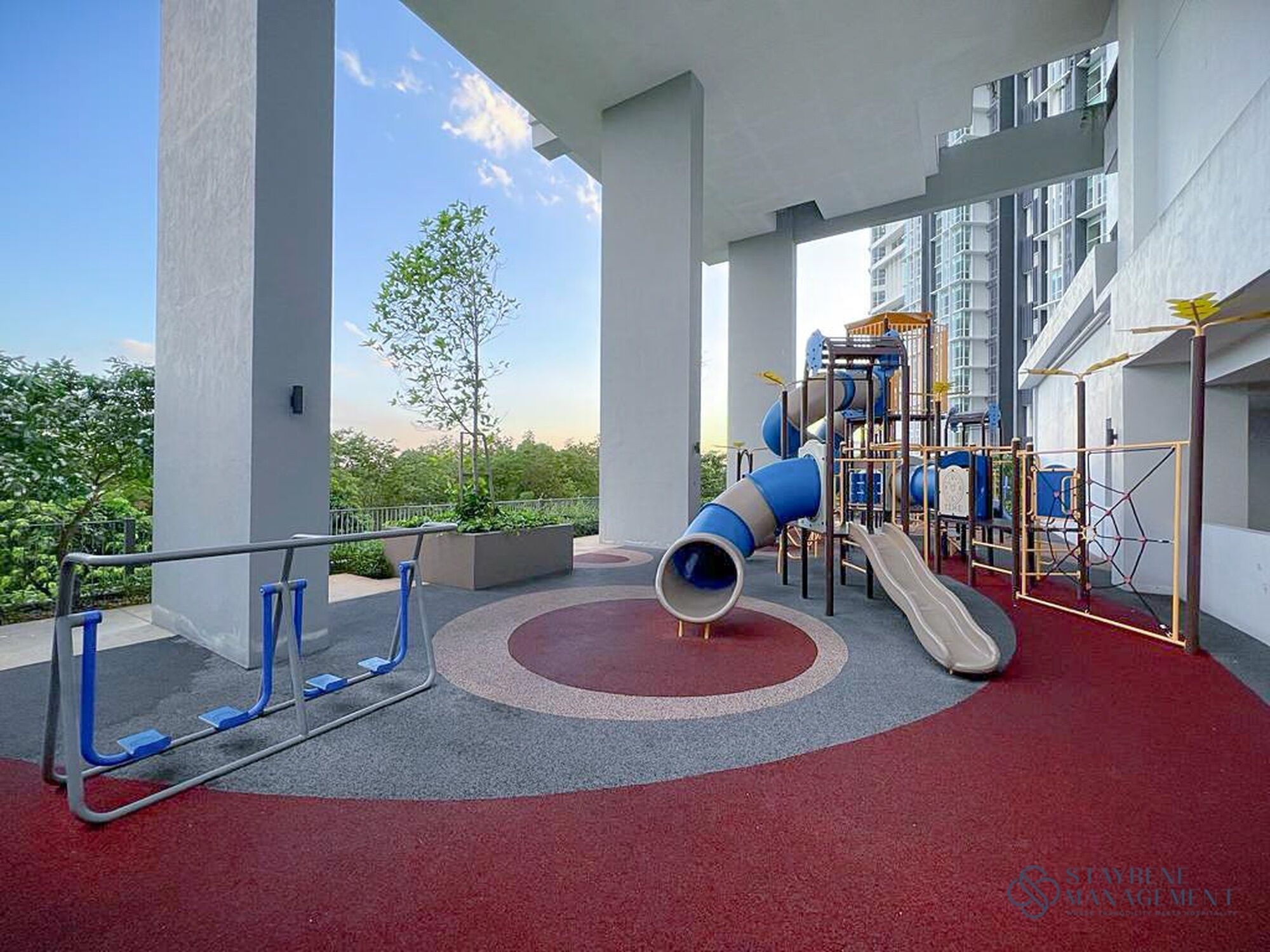A playground with slides and climbing structures, surrounded by a red carpet area and white pillars.
