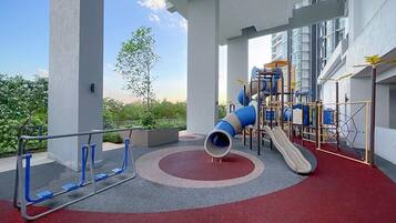 A playground with slides and climbing structures, surrounded by a red carpet area and white pillars.