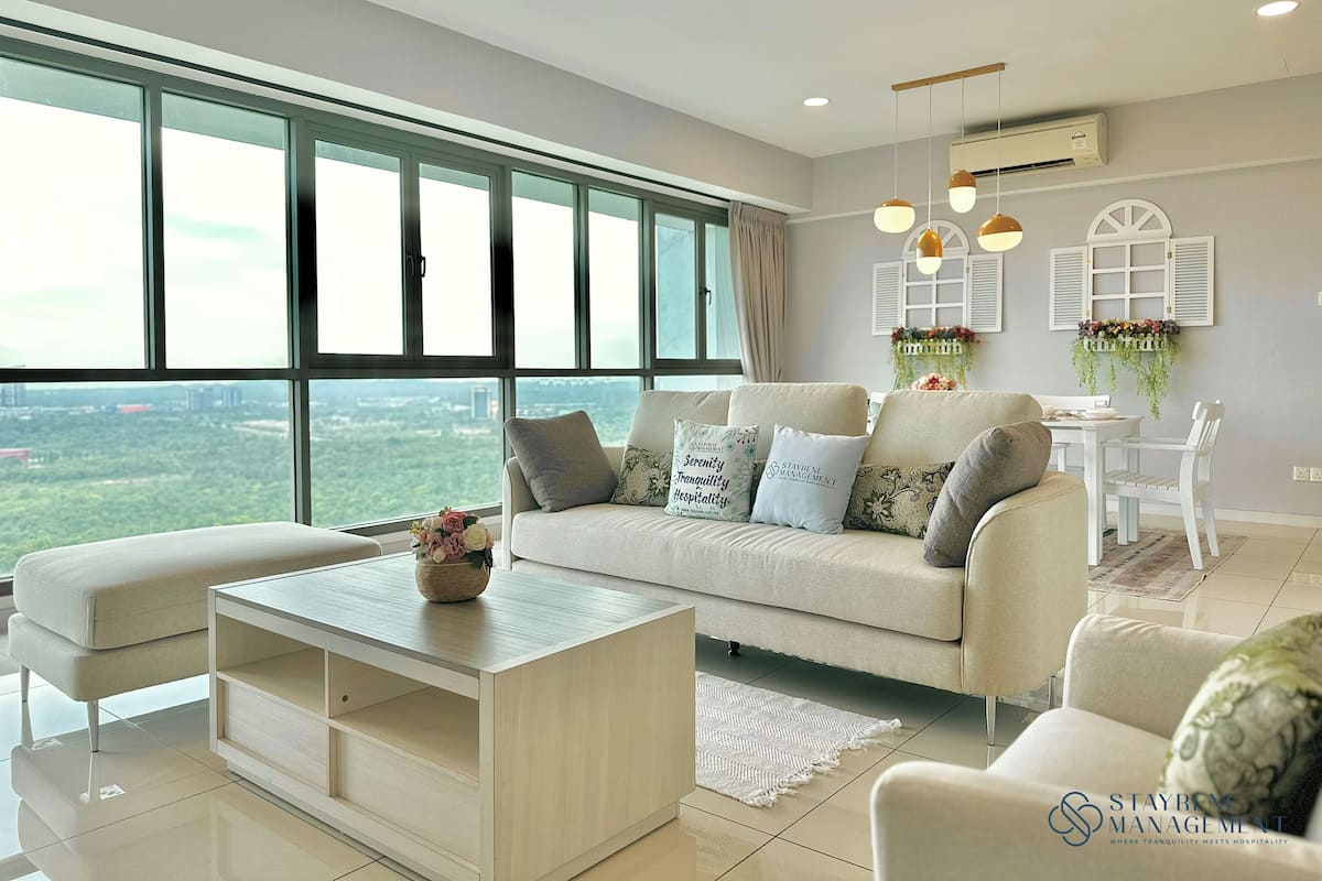 Uma sala de estar moderna com sofá, mesa de centro e cadeiras. Há uma janela grande com vista para a cidade, uma planta pendente e um ventilador de teto.