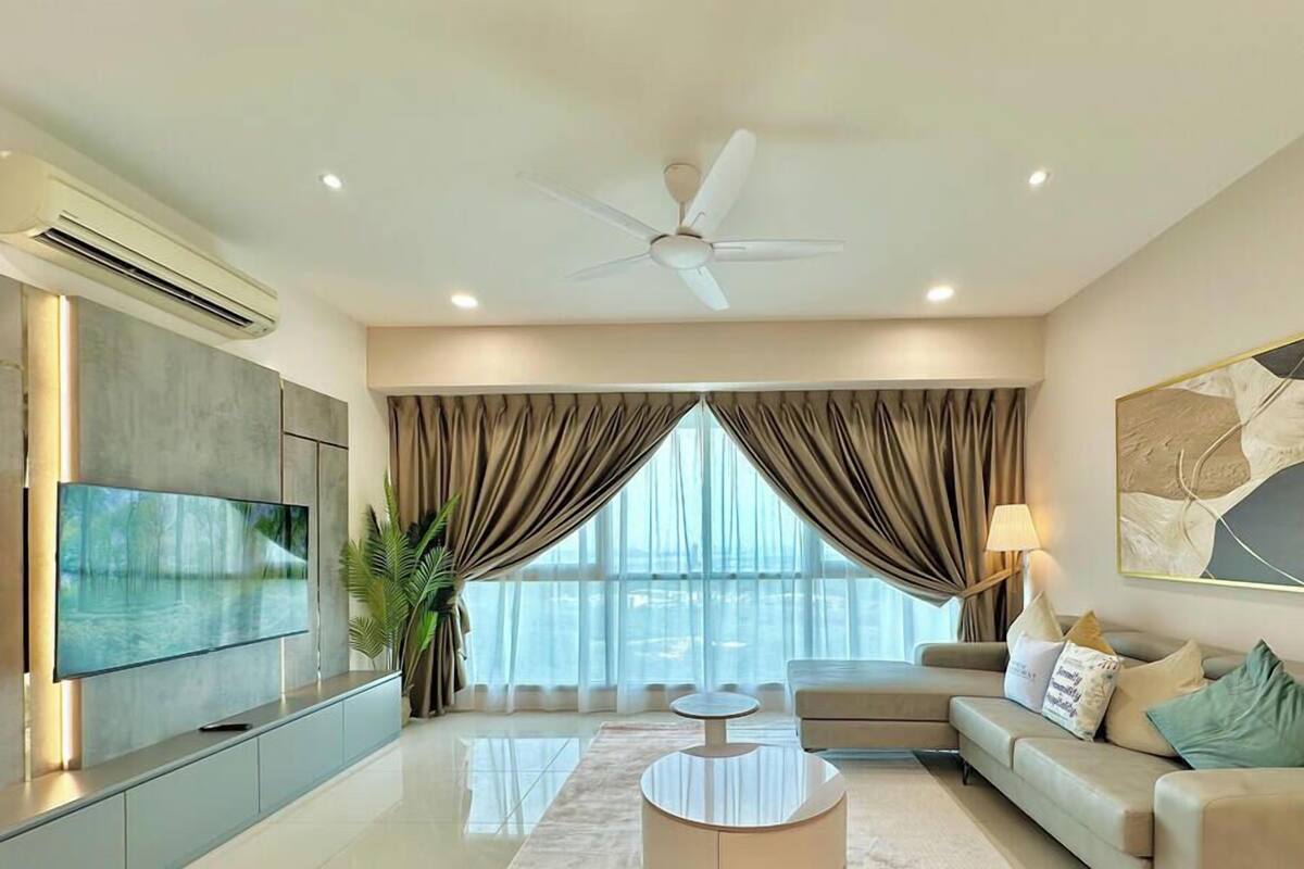 Uma sala de estar moderna com televisão de tela plana, ventilador de teto, sofá, mesa de centro e uma grande janela com cortinas.