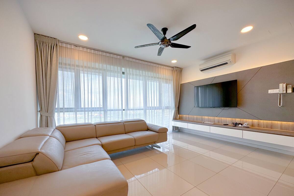 Uma sala de estar moderna com um sofá seccional bege, um ventilador de teto, uma TV de tela plana fixada na parede e um elegante console branco.