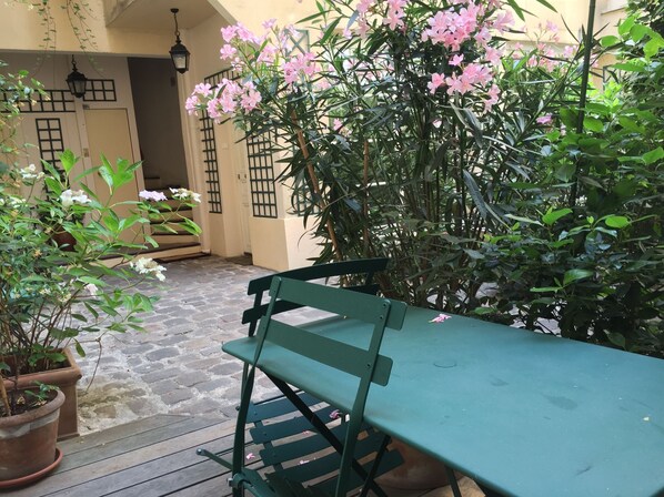 A courtyard with a green bench, potted plants, and a stone floor. - Duplex (ground floor and 1st floor - 2 bedrooms 2 bathrooms) -Center- Le Marais (Paris)