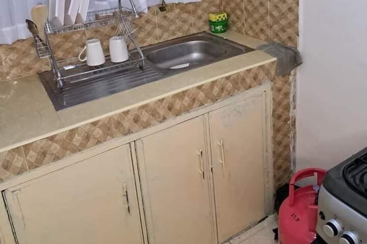 A kitchen with a sink, cabinets, a gas stove, and a gas cylinder.