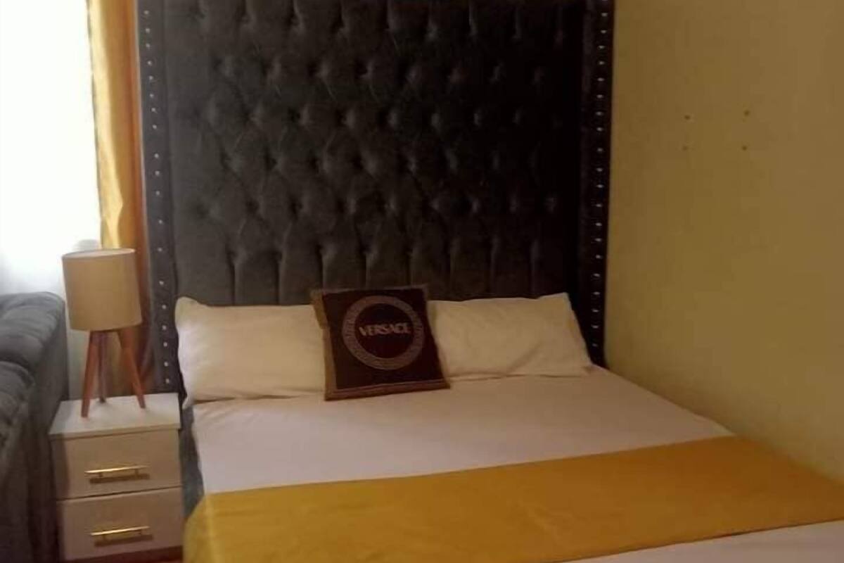 A hotel room with a large bed, a headboard, a bedside table, and a lamp.