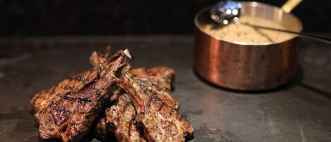 De la viande grillée et une marmite avec une louche, le tout posé sur une surface sombre.
