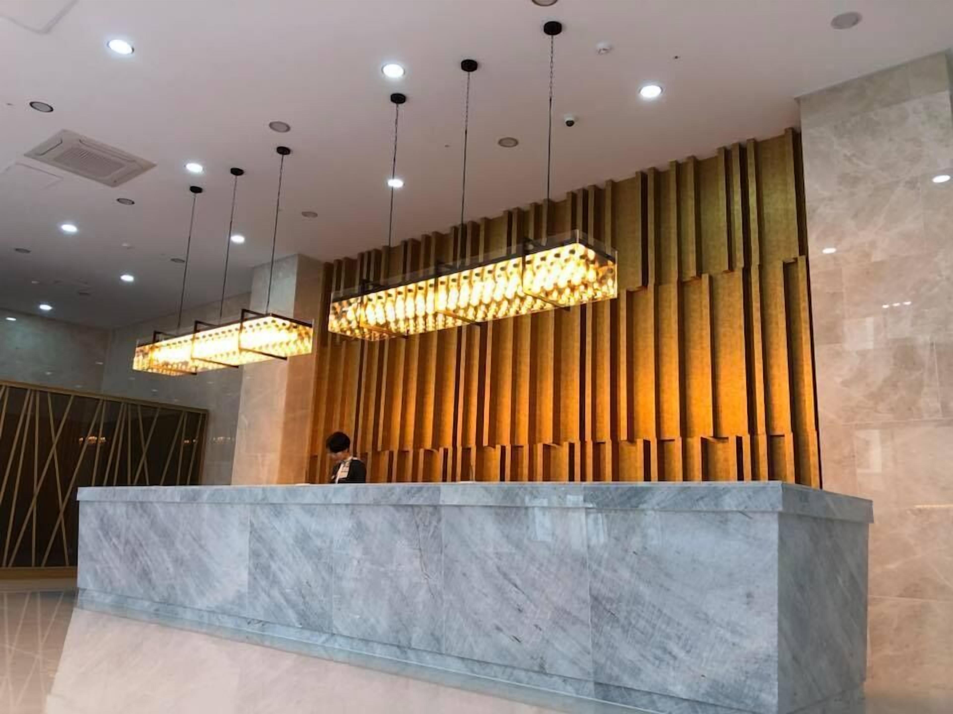 A reception desk with a marble top, wooden panel wall, and pendant lighting.