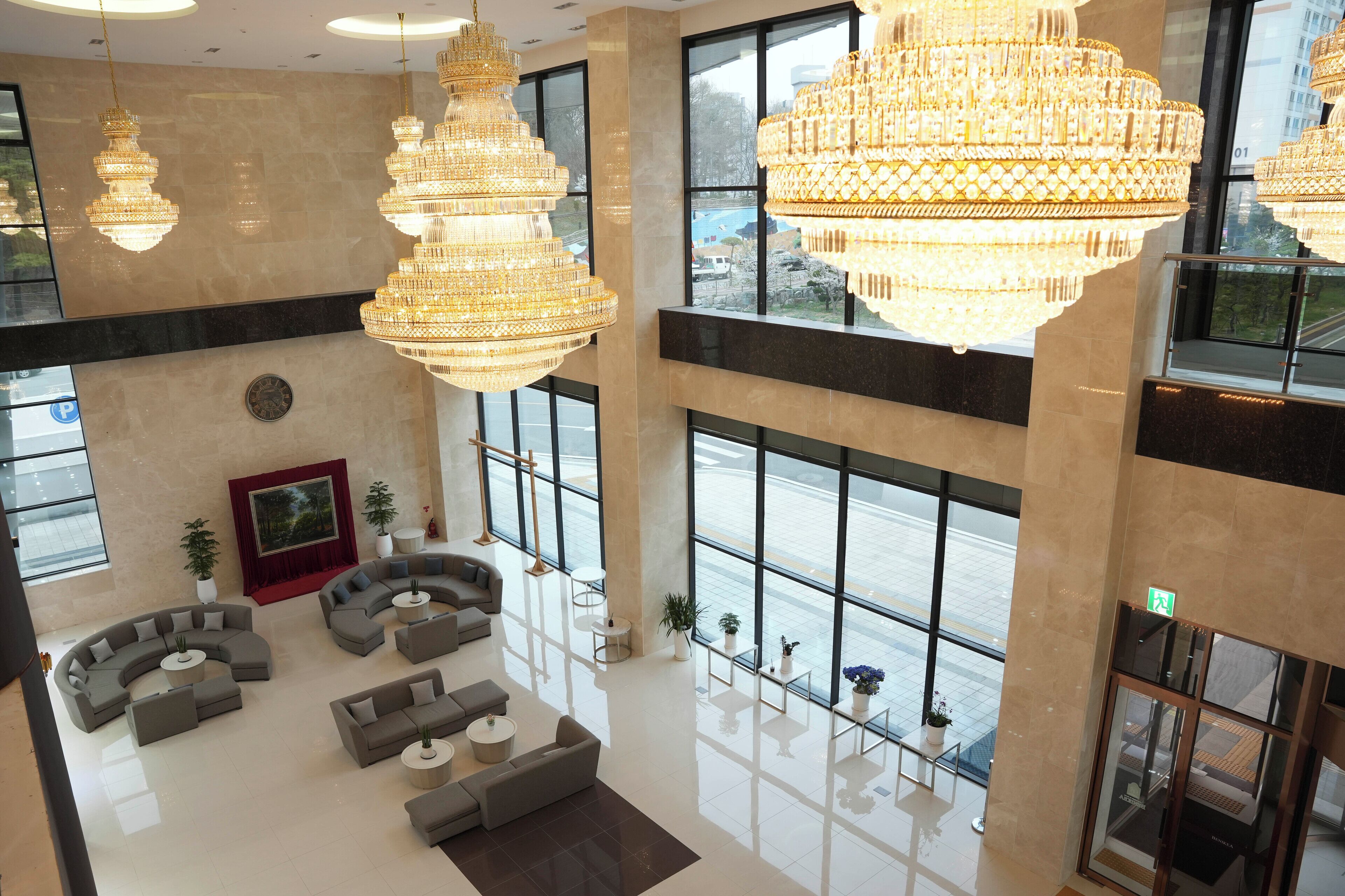 A spacious lobby with large chandeliers, a seating area with sofas and tables, and large windows offering views of the outside.