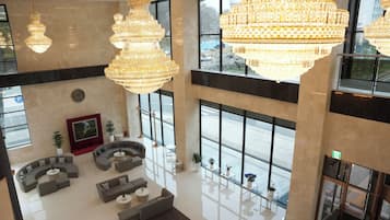 A spacious lobby with large chandeliers, a seating area with sofas and tables, and large windows offering views of the outside.