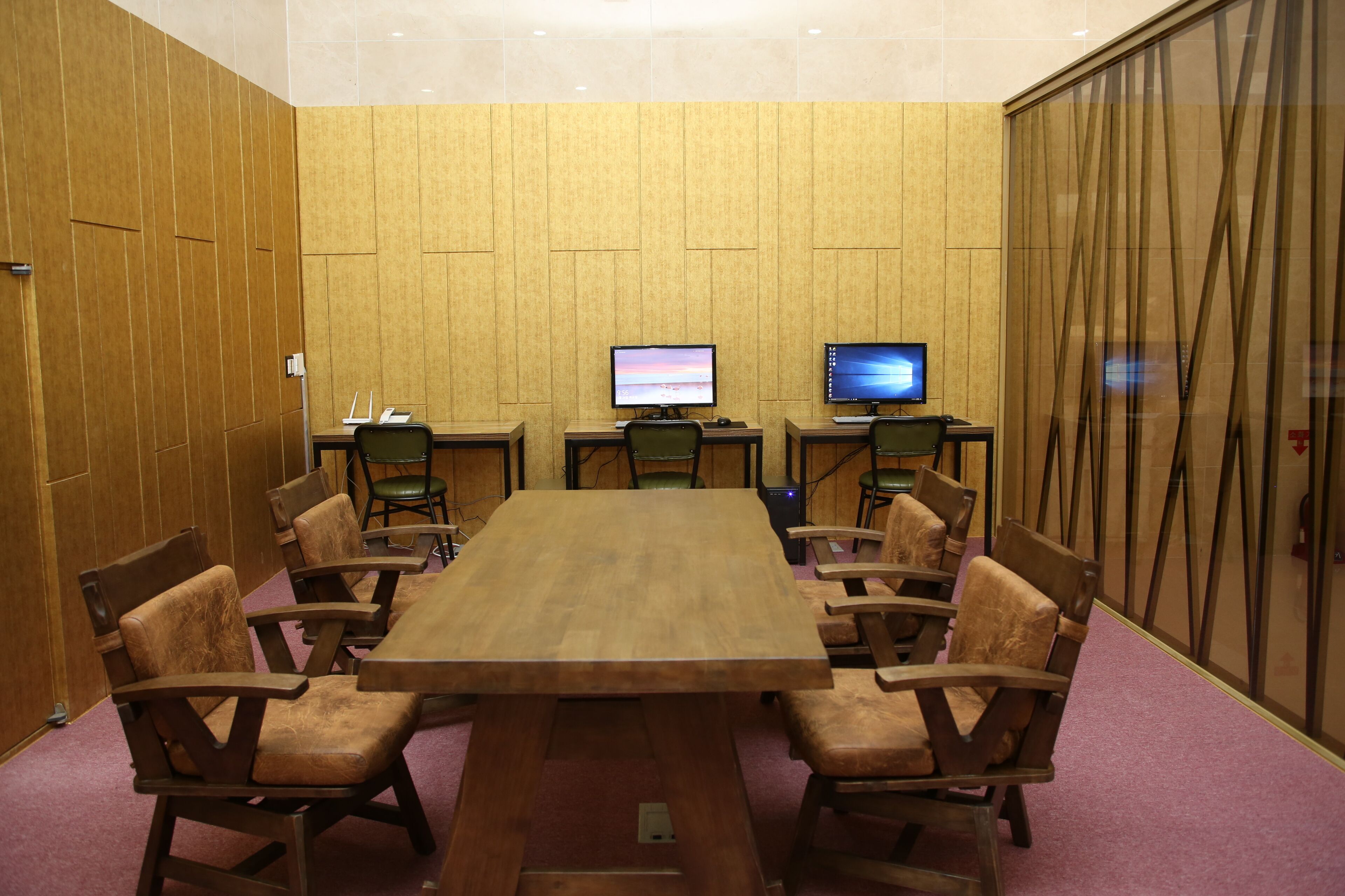 A conference room with a large wooden table, six chairs, two computer monitors, and a wooden paneled wall.