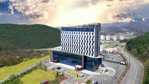 Un hôtel moderne à la façade en verre, situé dans une zone vallonnée, offrant une vue sur les bâtiments environnants et comprenant un parking.