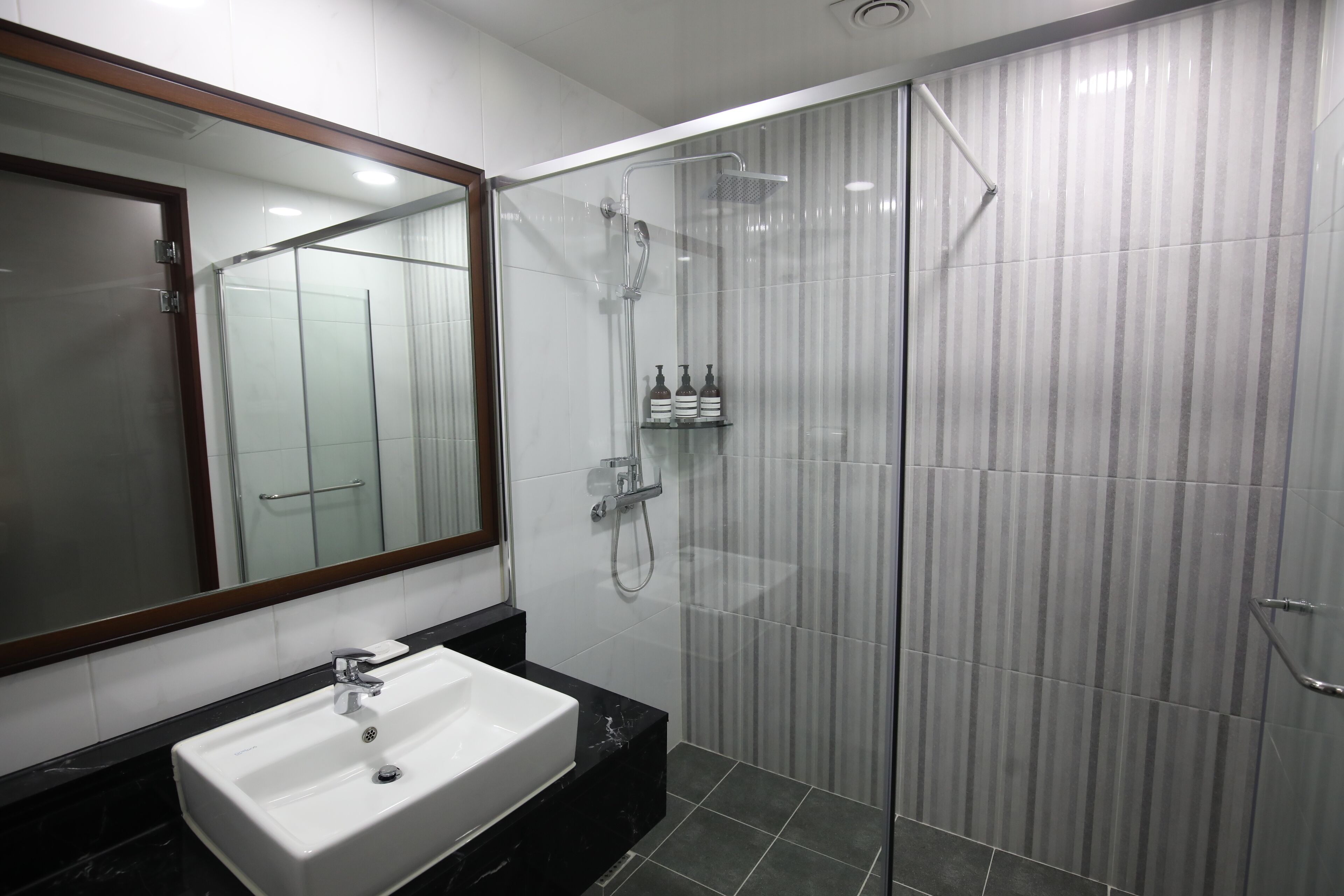 Un baño moderno con ducha envuelta en vidrio, un lavabo blanco y un espejo grande.