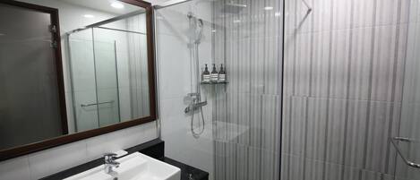 Un baño moderno con ducha envuelta en vidrio, un lavabo blanco y un espejo grande.