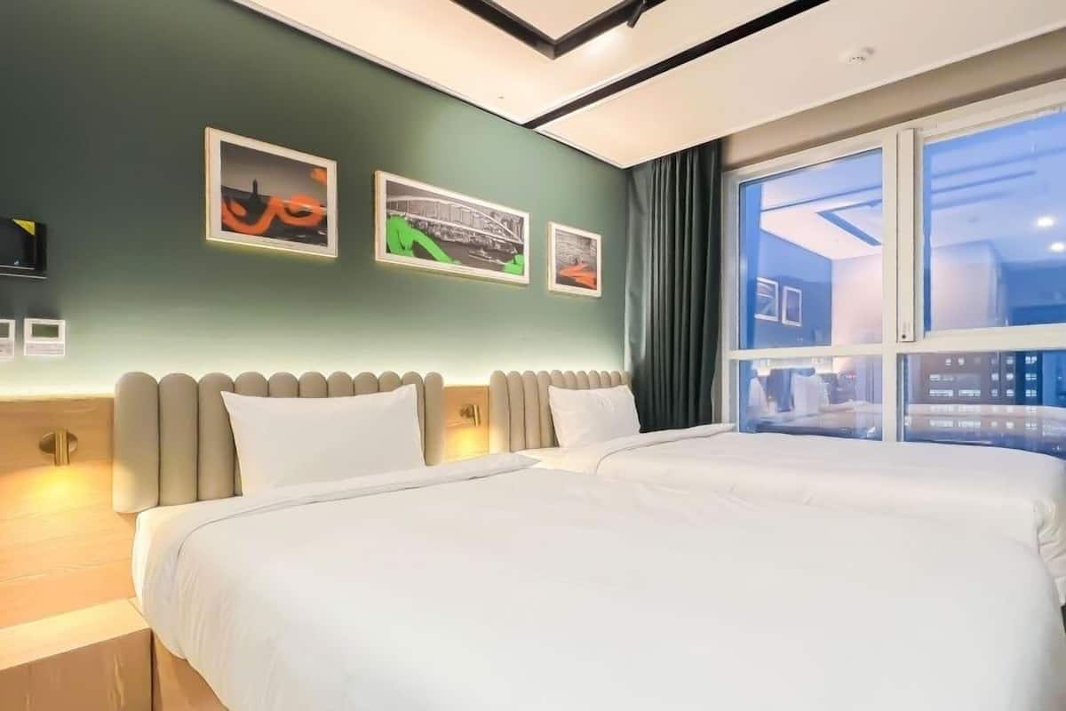 Habitación de hotel con dos camas, un ventanal grande y tres cuadros en la pared.