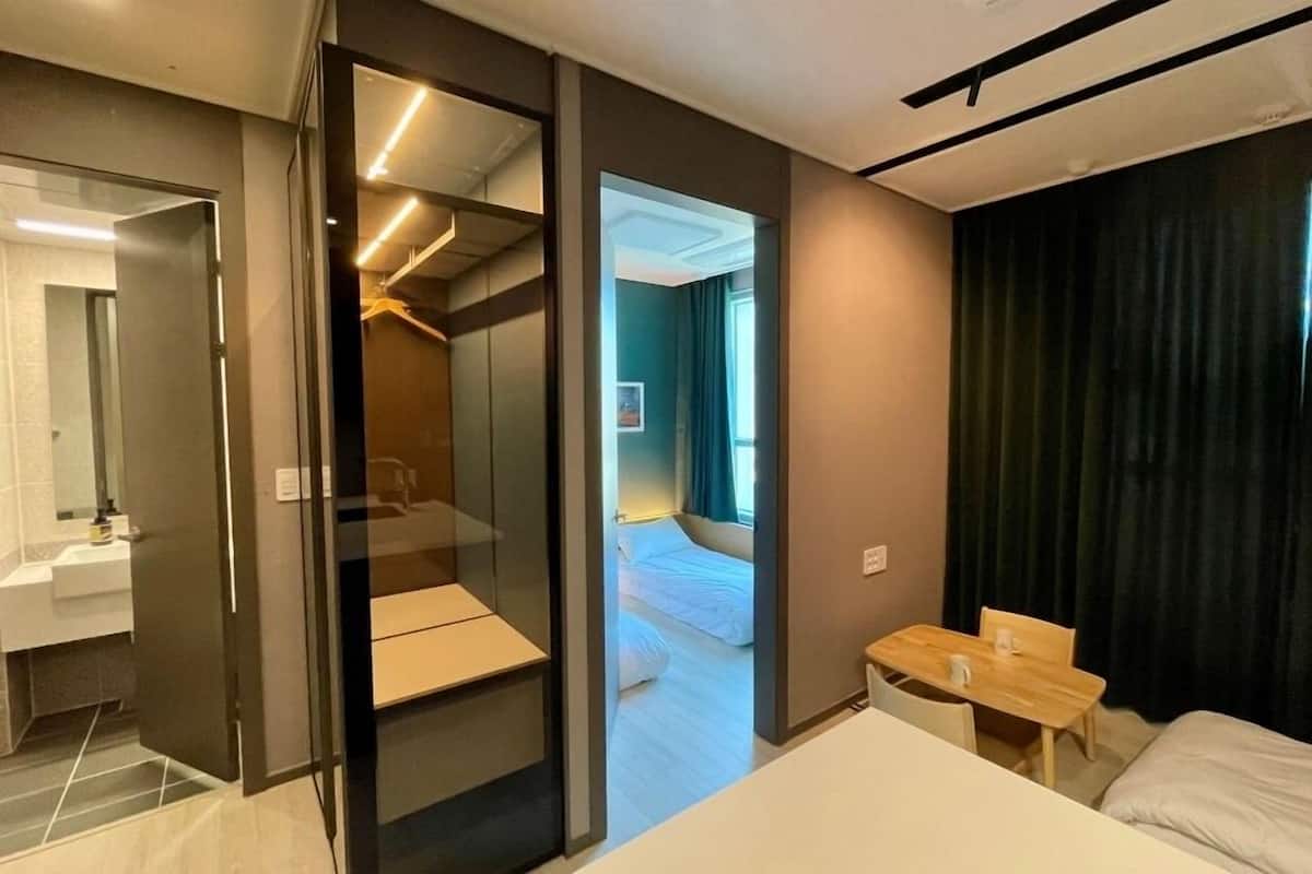 Una habitación de hotel moderna con una cama, una pequeña mesa de madera, un espejo y un vestidor.