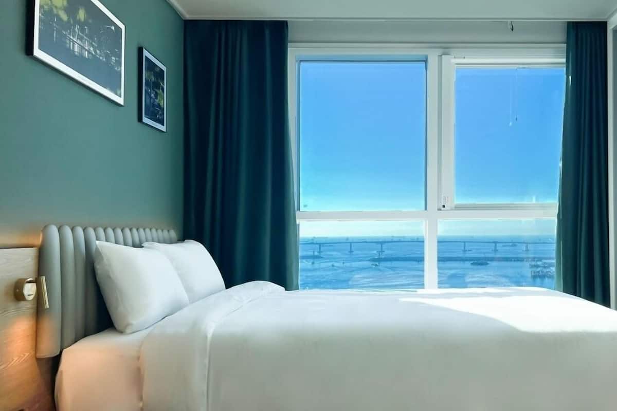 Habitación de hotel con una cama grande, vistas de la ciudad a través de un ventanal y un radiador en la pared.