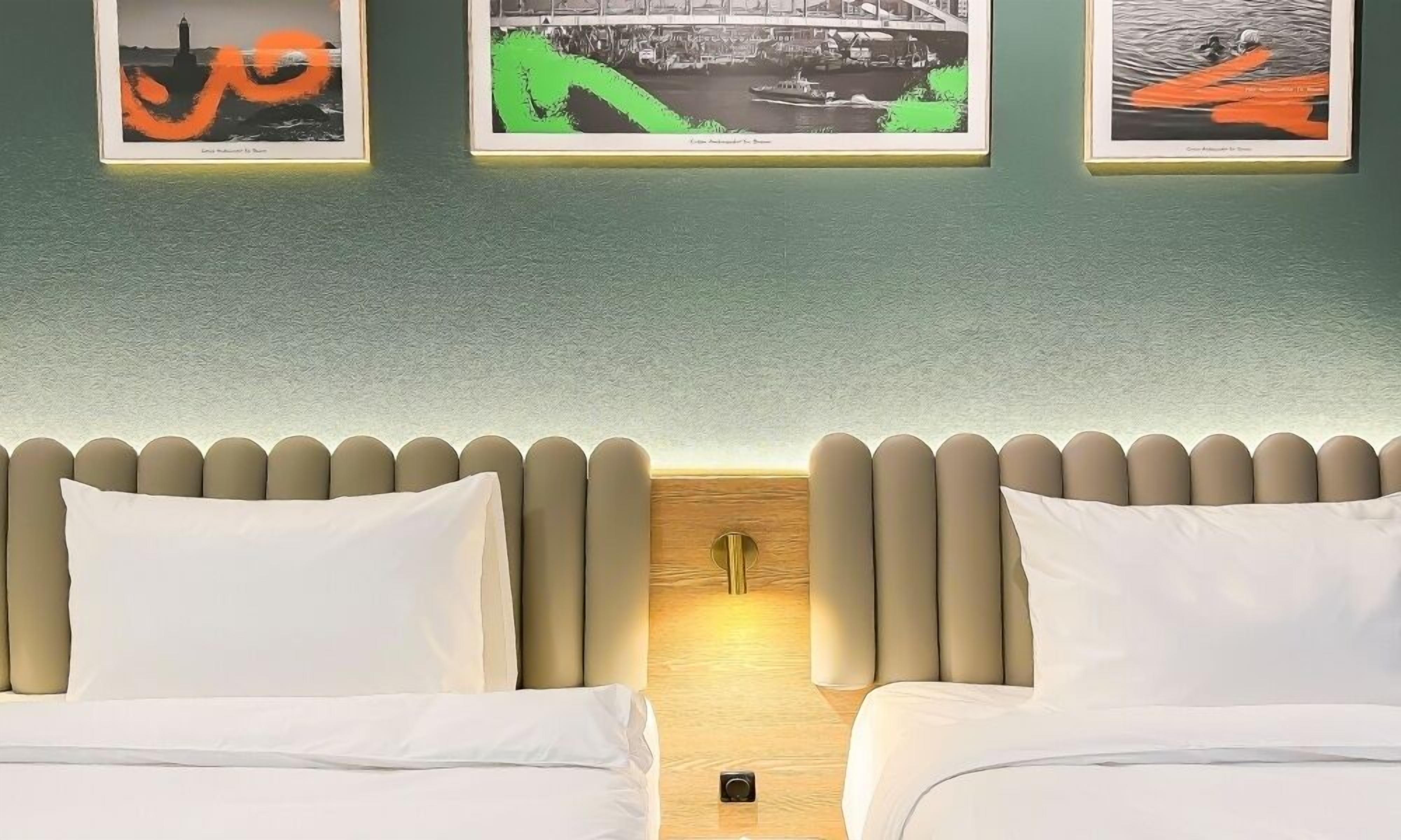 Una habitación de hotel con dos camas, un cabecero de madera y tres cuadros en la pared.