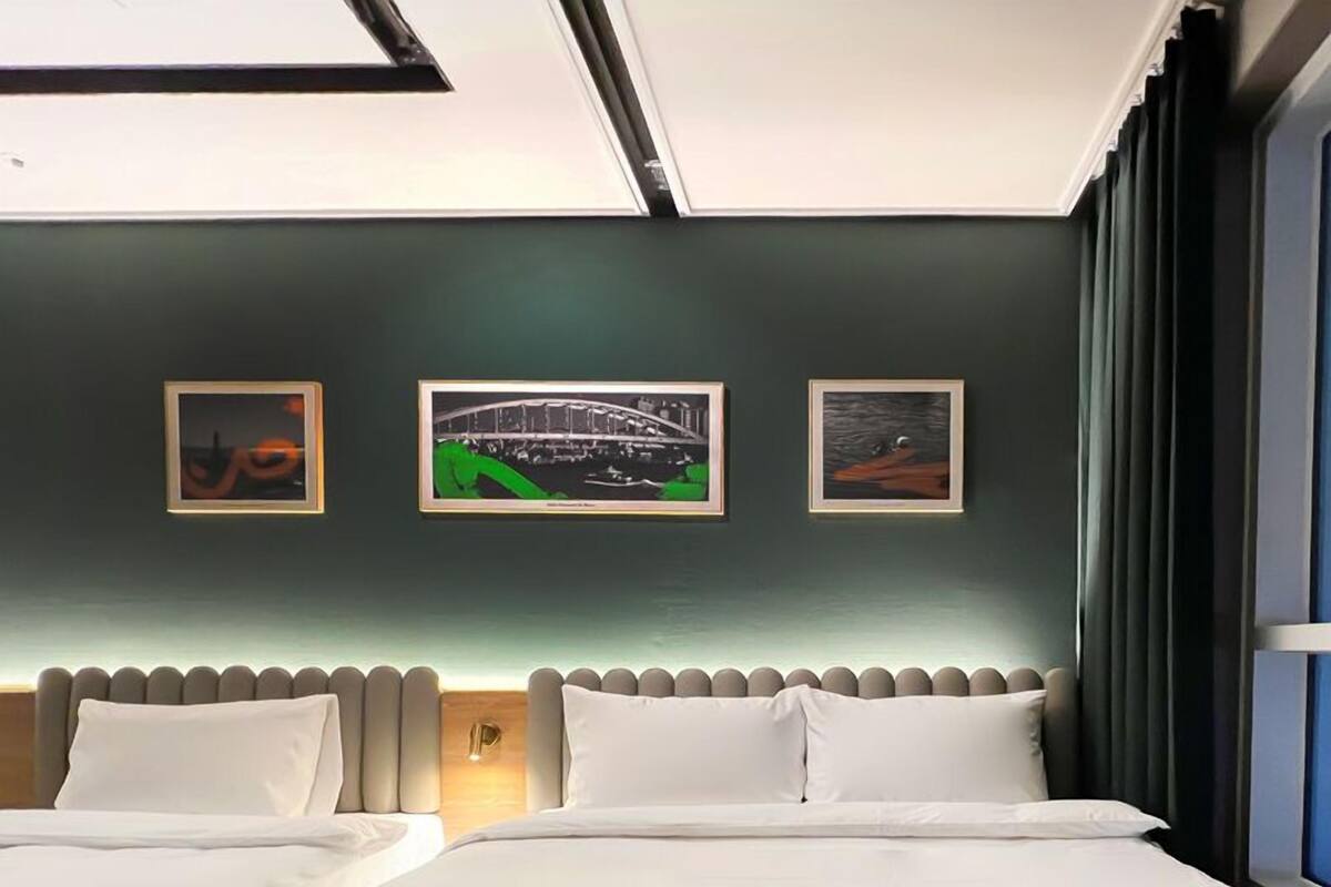 Habitación de hotel con dos camas, un cabecero y tres cuadros en la pared.