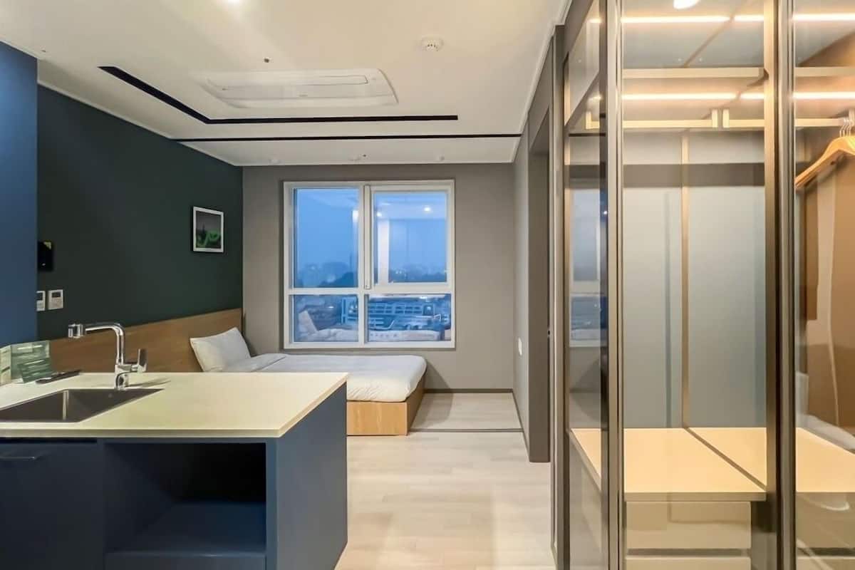 Una habitación de hotel moderna con un ventanal grande, una cama, una mesita de noche y un box de ducha de vidrio.