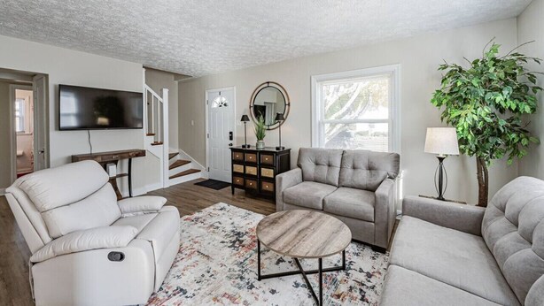 Un salon comprenant un canapé, des fauteuils, une table basse, un téléviseur, un escalier et une plante.