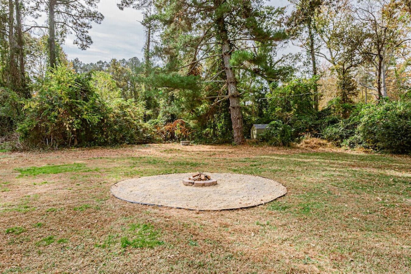 A circular fire pit in a grassy yard surrounded by trees and shrubs.