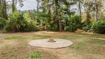 A circular fire pit in a grassy yard surrounded by trees and shrubs.