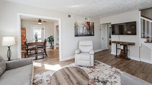Un salon spacieux comprenant un coin repas, un fauteuil blanc et un grand tableau accroché au mur.